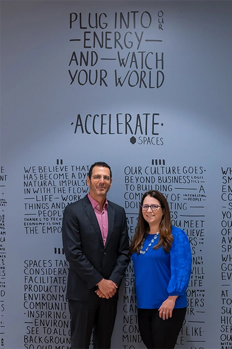 Man and woman standing against a blue wall with writing on the wall 