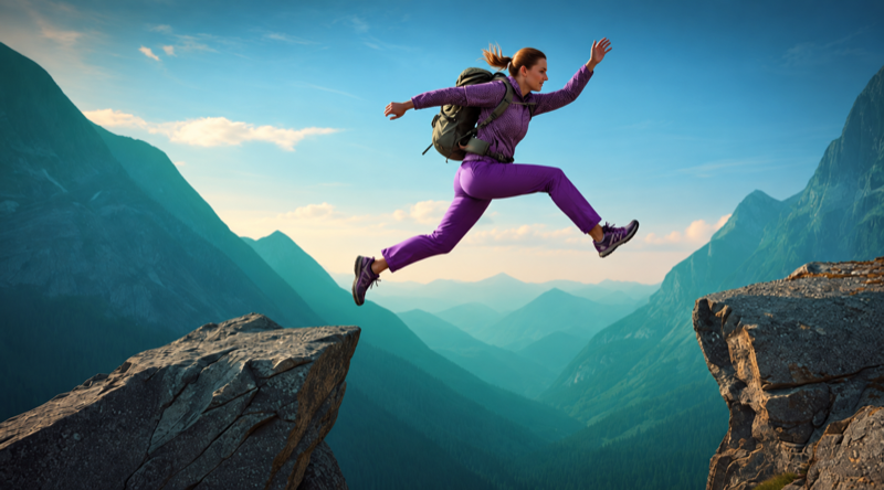 A hiker leaping across the gap between two mountain ledges